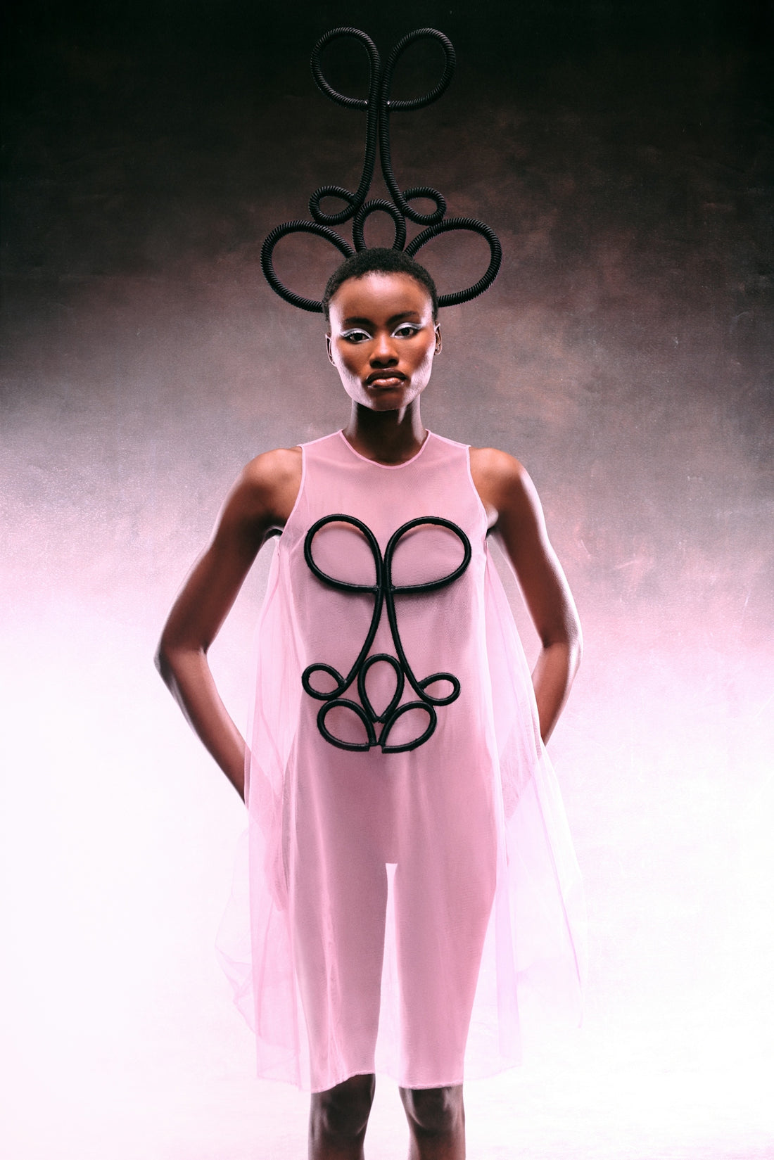 Woman models a pink dress with an ornate black headdress.