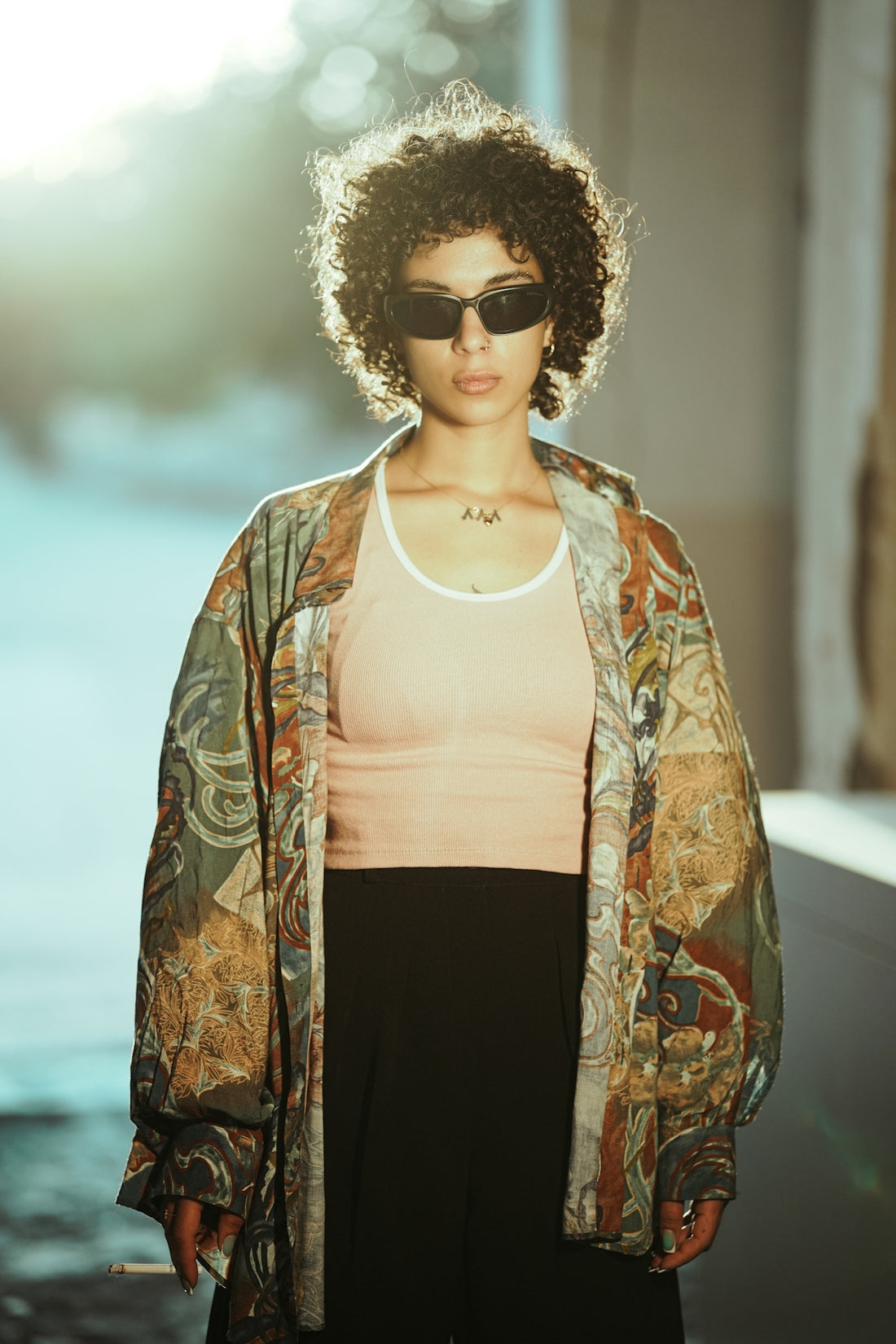 Woman with curly hair wearing sunglasses and patterned jacket.