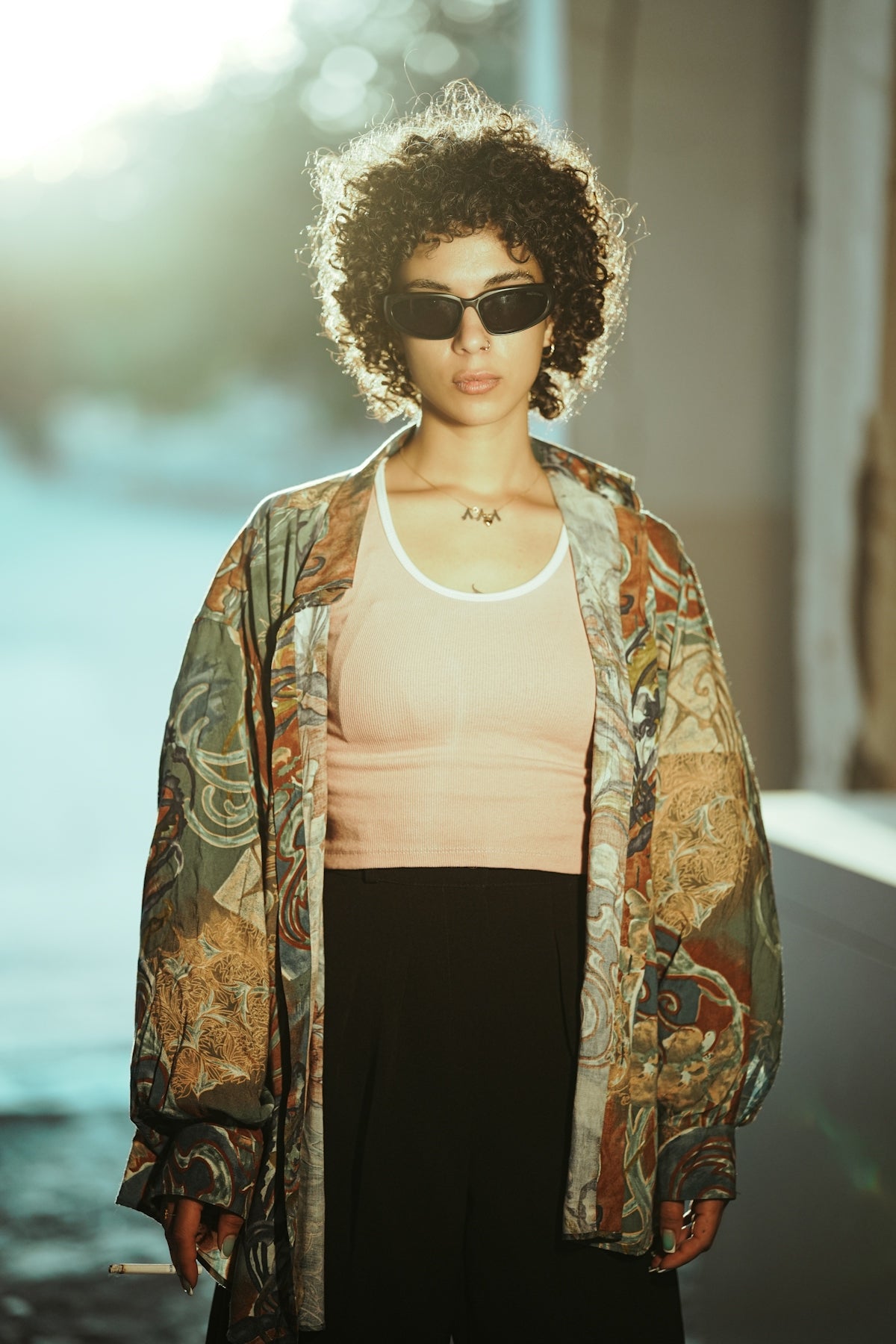 Woman with curly hair wearing sunglasses and patterned jacket.