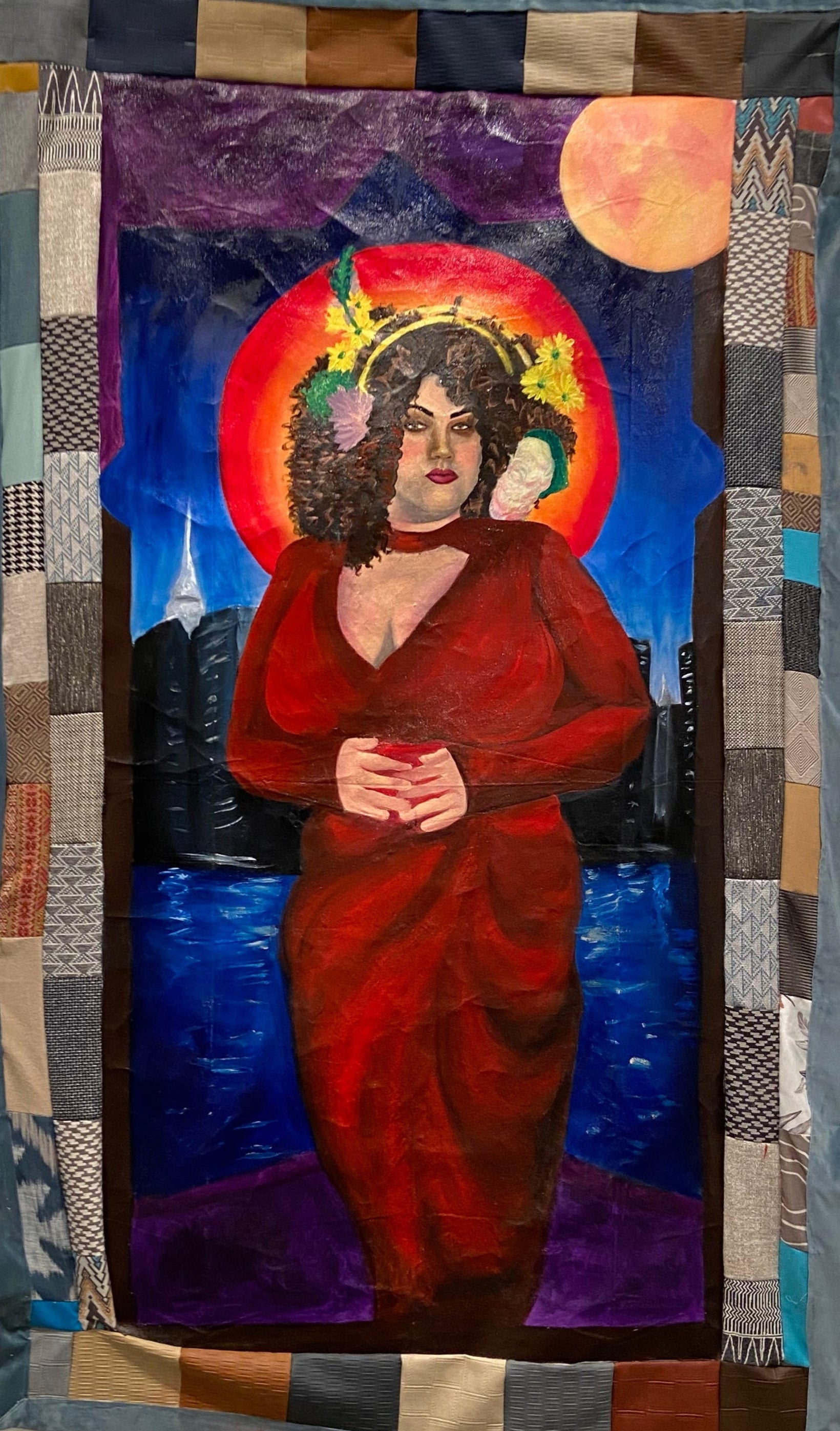 Patchwork tapestry with a central figure in a red robe on a white wall