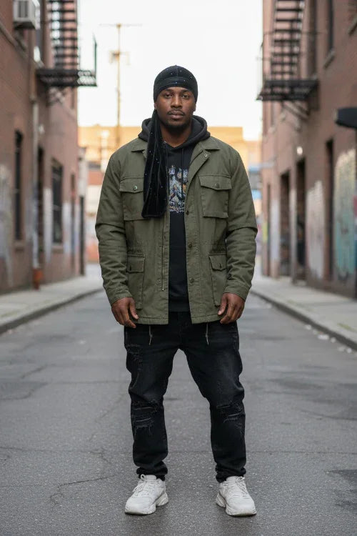 Man wearing a green jacket and black pants standing on an urban street.