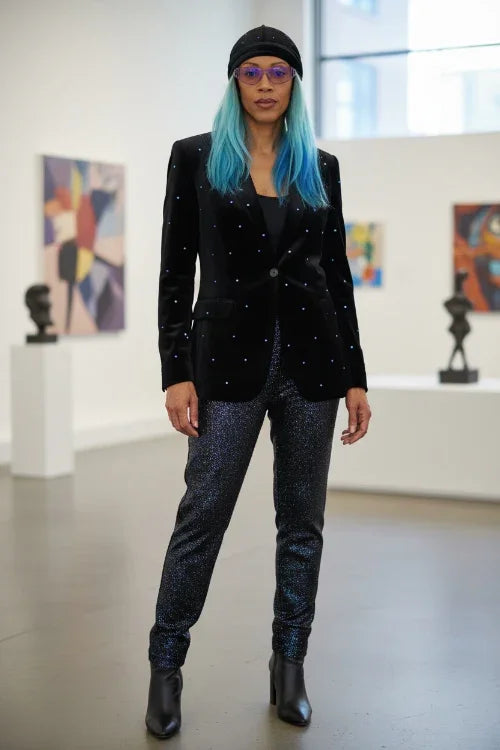 Person wearing a black blazer with sparkling details, black pants, and black boots in an art gallery.