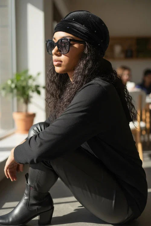 Woman in black outfit and sunglasses squatting indoors